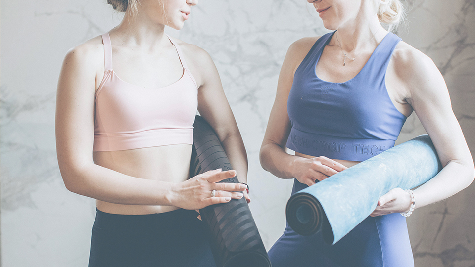 Zwei Personen mit der Yogamatte unter dem Arm unterhalten sich.